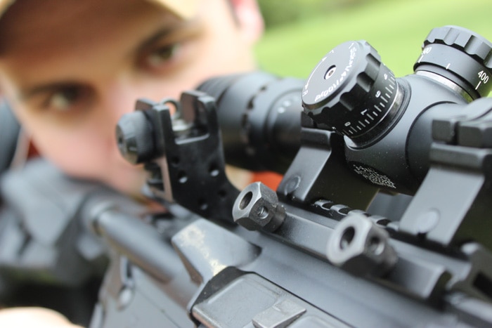 sight focused view of man shooting scoped rifle