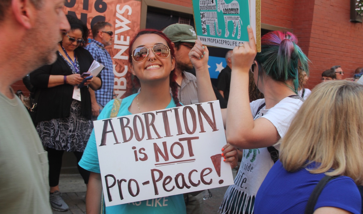 The woman holding the sign "abortion is not pro-peace!" passed through a crowded street with three other women advocated feminist ideas. 