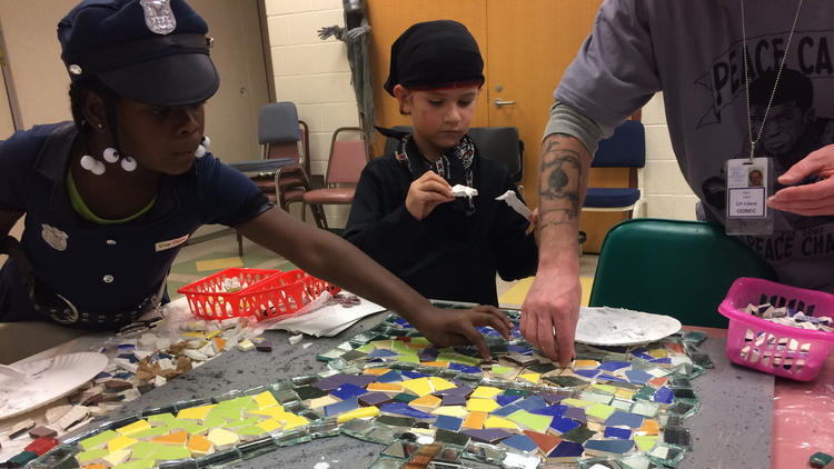 Ariyonna Pritchett, left, and Sebastian Taylor, middle, help a volunteer build a peace-themed mosaic featuring toy guns traded in for peaceful prizes. (Photo: Erin Cox / Baltimore Sun)