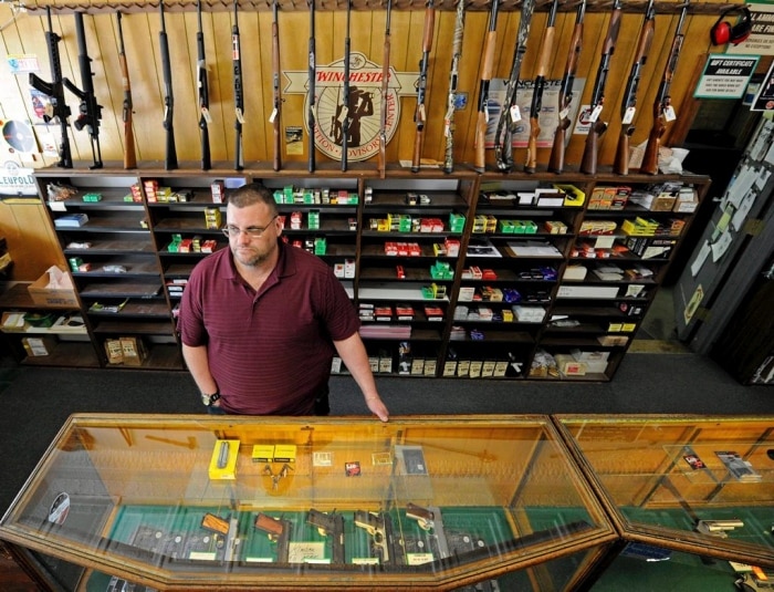 Keith Savage stands at the counter of his gun shop, Braverman Arms, in Wilkinsburg. Savage tells The Citizens Voice newspaper he doesn’t think the Pennsylvania Instant Check System works and goes down too frequently. (Photo: Connor Mulvaney/ PublicSource)