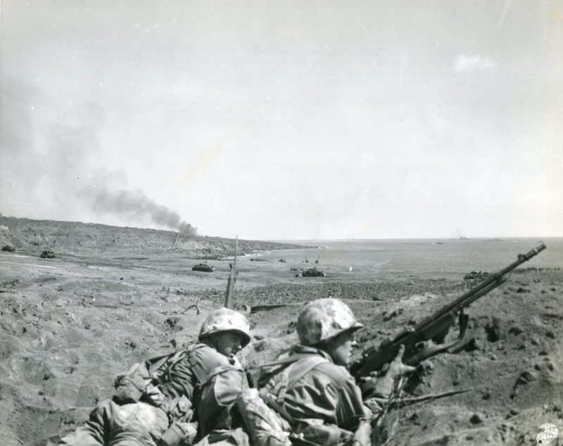 "FAITHFUL AND WAITING----While a gigantic artillery and tank battle rages behind them on the Iwo Jima beachhead, Marines (left to right) PFC Joseph de Blanc, of Union, Maine, and PFC Frank Hall, of Reed W. Virginia, faithfully wait for orders in a shell hole.” Note the M1918 Browning Automatic Rifle (BAR).