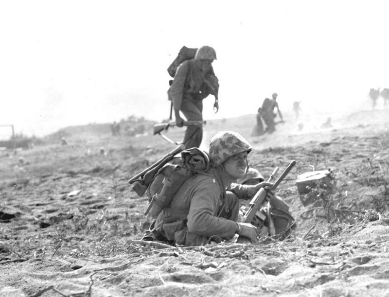 “GOING INLAND--- Determination written on their countenances, Marines start the drive to the interior of Iwo Jima. Running at a crouch, they dart across the table and in the shadow of Mount Suribachi, taking advantage of the scant protection offered by small rises in the volcanic sand." Note the M1 Carbine of the Marine in the foreground, with a rifle grenade attachment installed, and the Devil Dog with a Winchester Model 12 trench gun in the background.