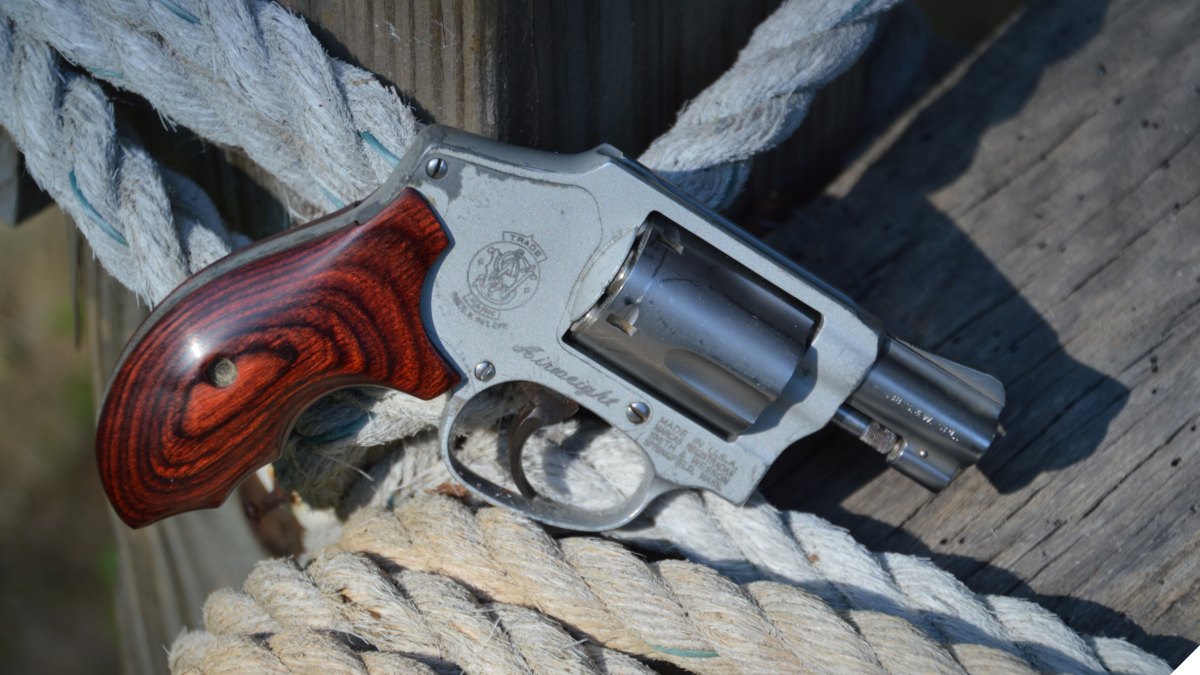 A Smith & Wesson Model 642 J-frame snub-nosed .38 Special revolver rests on a pile of rope atop a wooden bench.