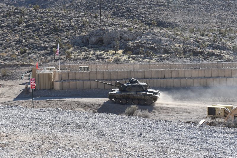 M60 battle tank driving around a tan Hesco barrier compound