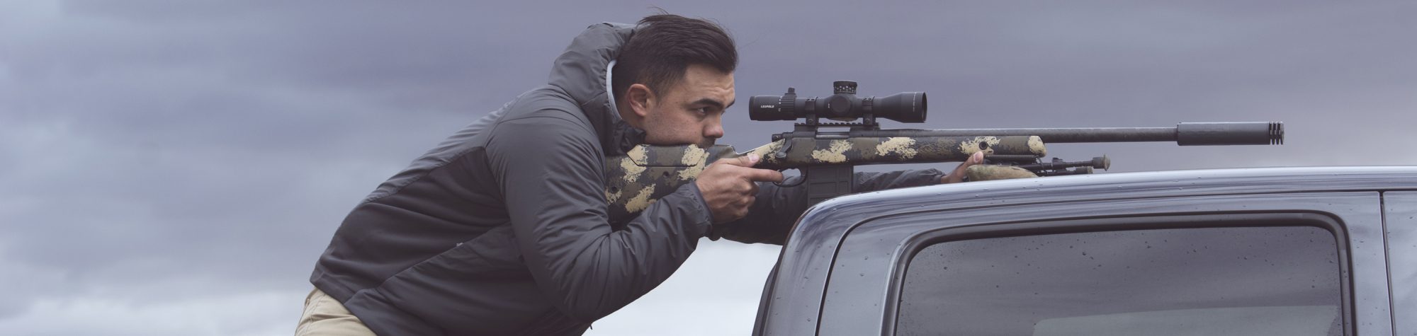 A man aims a rifle through a Leupold Mark 5HD scope on a bolt-action rifle