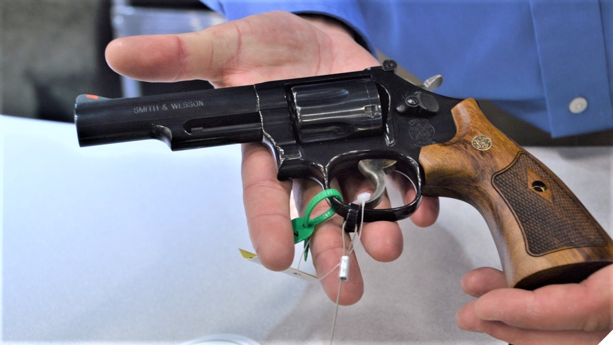 A man holds a beautifully blued S&W K-frame Model 19 .357 Magnum revolver with wood grips