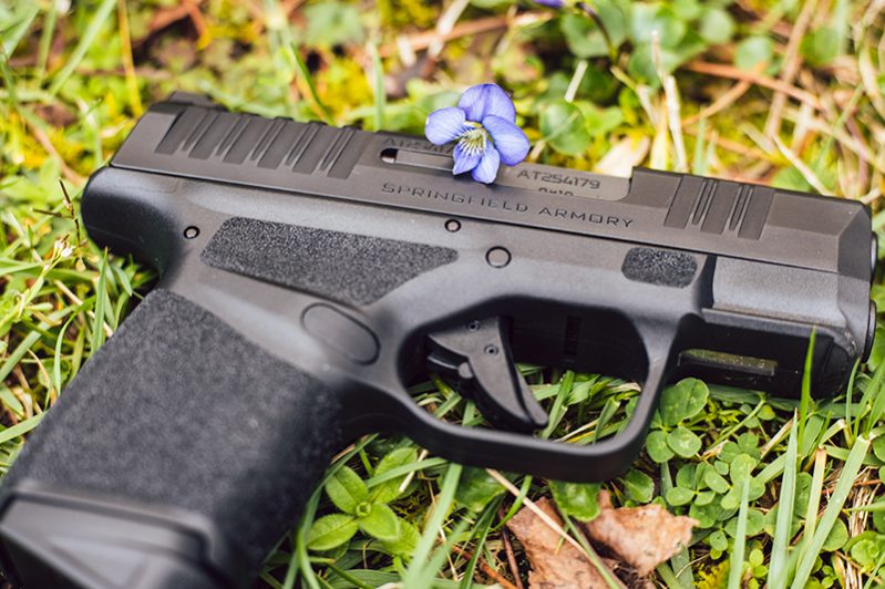 A Springfield Armory Hellcat pistol in a green field of clover with white briar flowers