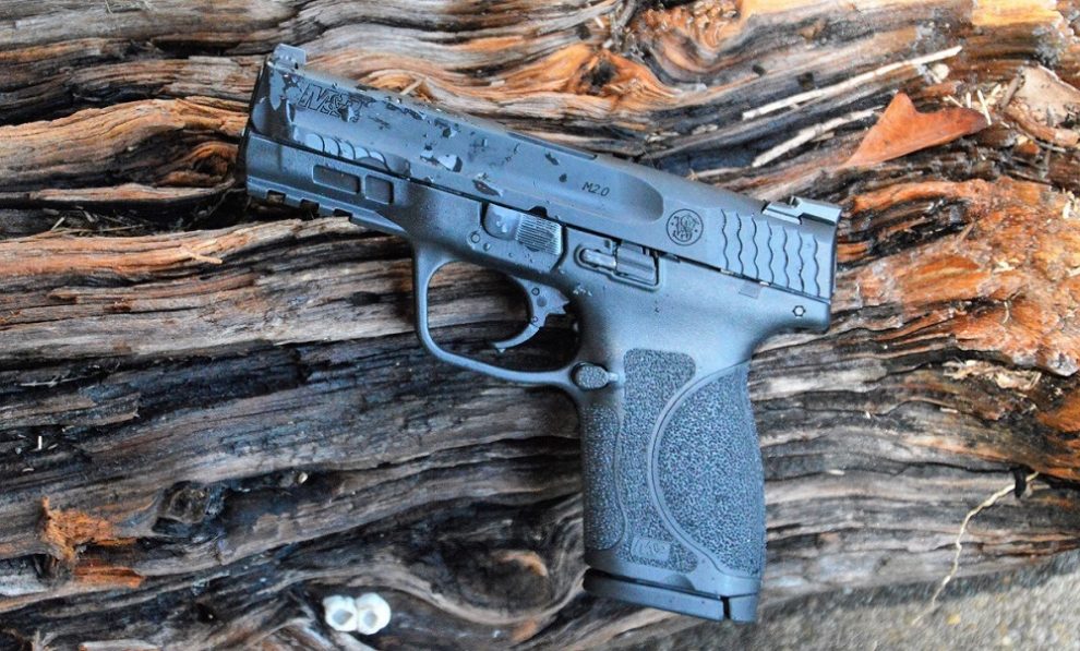 A Smith & Wesson M&P M2.0 Compact on a timber block, freckled with water