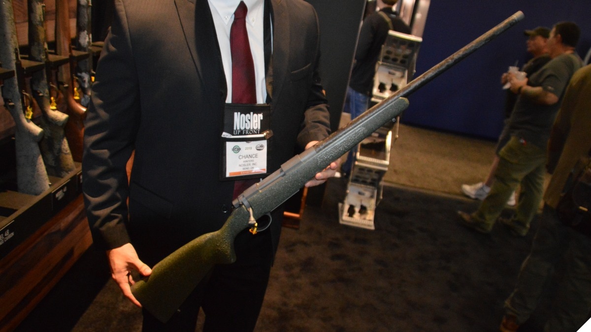 A man in a suit holds a bolt-action Nosler rifle