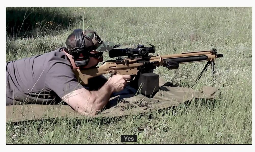 A man shoots a belt-fed machine gun while standing up