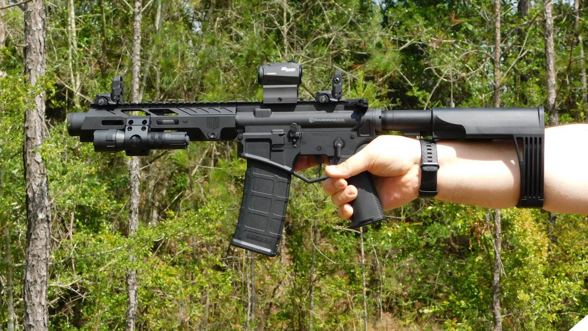 An AR-15 pistol with a pistol brace held outstretched in a man's hand