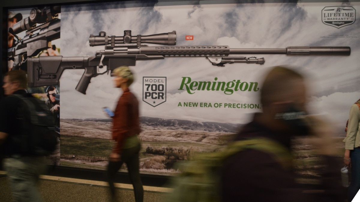 People walk in front of a Remington sign at a firearms trade show